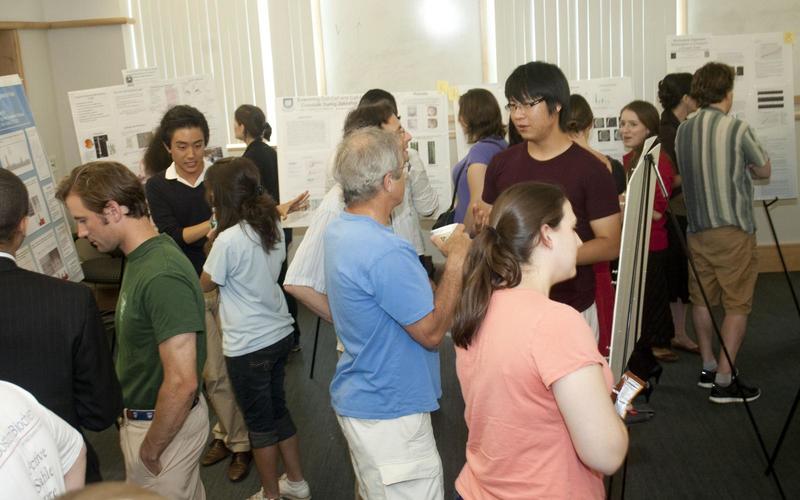 Large group of people talking with one another with posters around the perimeter of the room