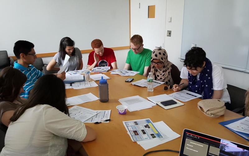 Students sitting around a large table reading a paper during a group activity