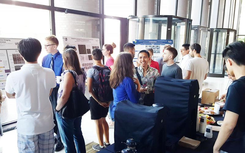 Large group of people talking with one another with posters around the perimeter of the room