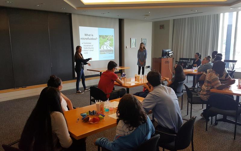 Two presenters point to a slide during a powerpoint presentation in front of a large group