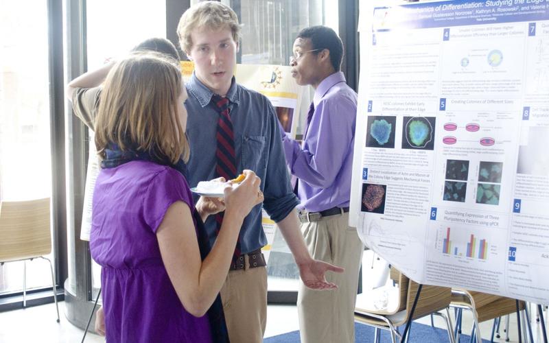 Undergraduate student talking to a visitor in front of his poster