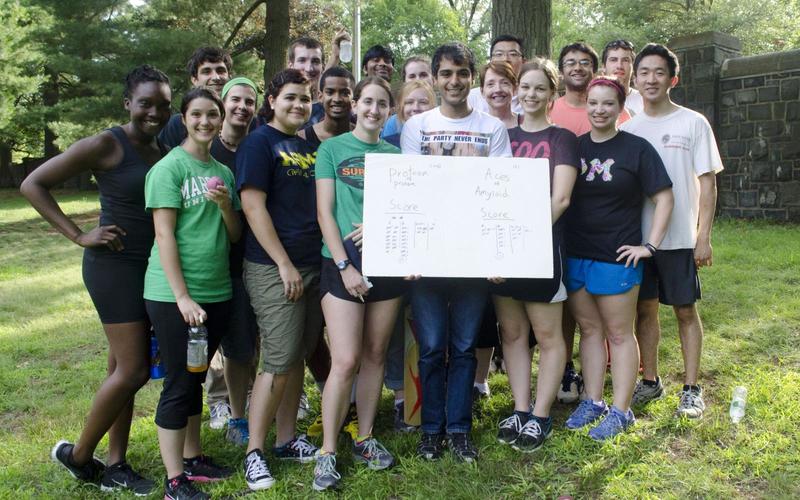 REU students and leadership group in athletic clothes holding a badminton scoreboard