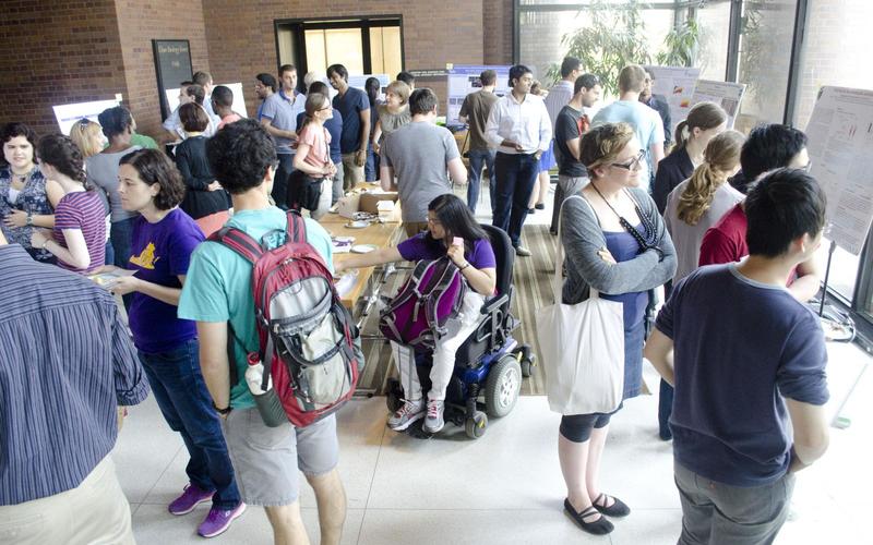 Large group of people talking with one another with posters around the perimeter of the room