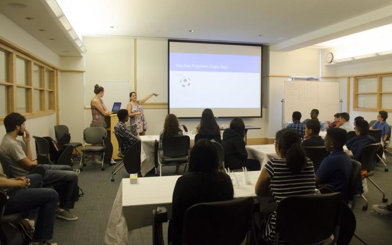 Two presenters point to a slide during a powerpoint presentation in front of a large group