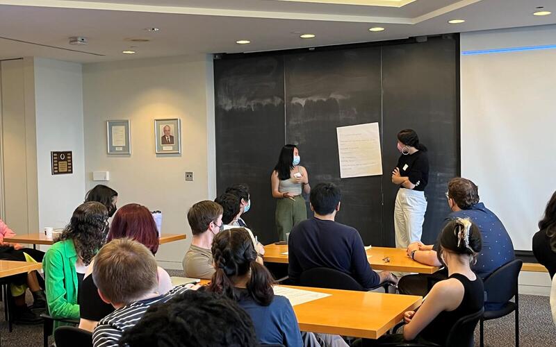 Two presenters stand in front of a large piece of poster paper