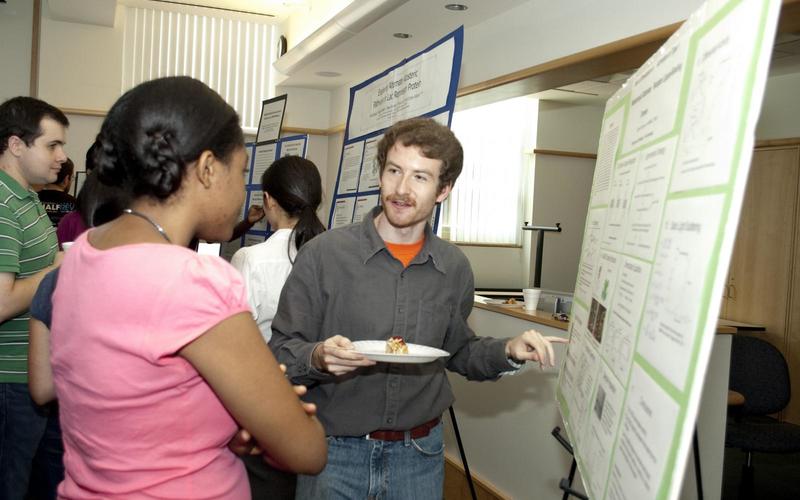 Undergraduate student talking to a visitor in front of his poster