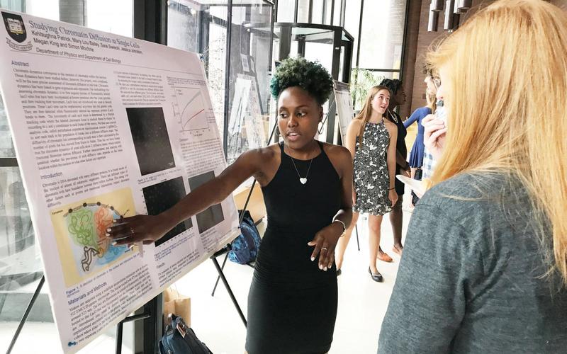 Undergraduate student talking to a visitor in front of her poster