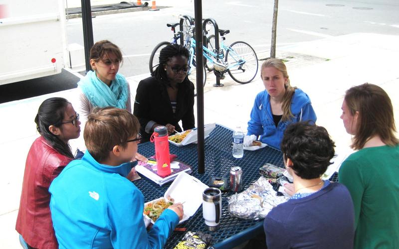 Group of people sit around a picnic table talking and eating lunch