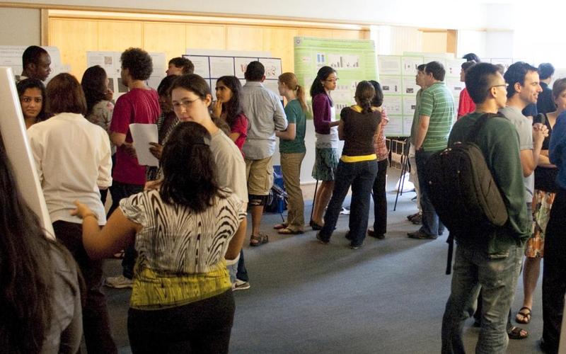 Around 15 people in a large room with posters on the perimeter of the room