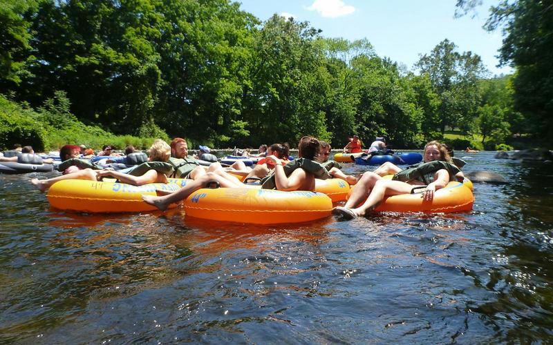 Group of REU students in lifejackets sitting in inner tubes and holding hands as they float down a river