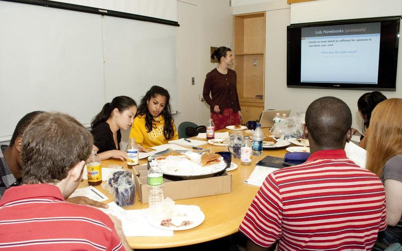 Students sitting around a large table while one presents a powerpoint at the head of the table