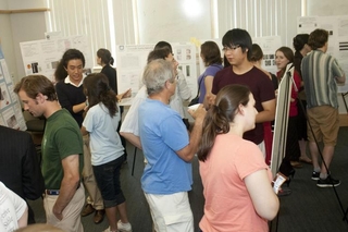 Large group of people talking with one another with posters around the perimeter of the room