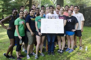 REU students and leadership group in athletic clothes holding a badminton scoreboard