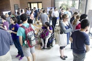 Large group of people talking with one another with posters around the perimeter of the room