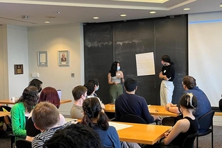 Two presenters stand in front of a large piece of poster paper