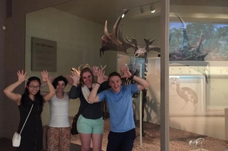 Group of 4 REU students standing in front of a moose using their hands to mimic moose antlers