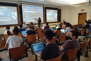 PEB graduate student points to a line of code while REU students code along on their own computers
