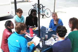 Group of people sit around a picnic table talking and eating lunch