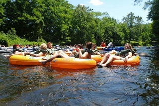 Group of REU students in lifejackets sitting in inner tubes and holding hands as they float down a river