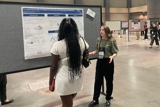 Karah standing in front of her research poster at LANS talking with a visitor