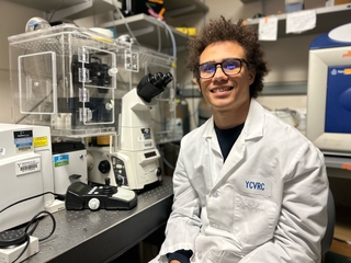 Shaka in the lab next to a microscope setup